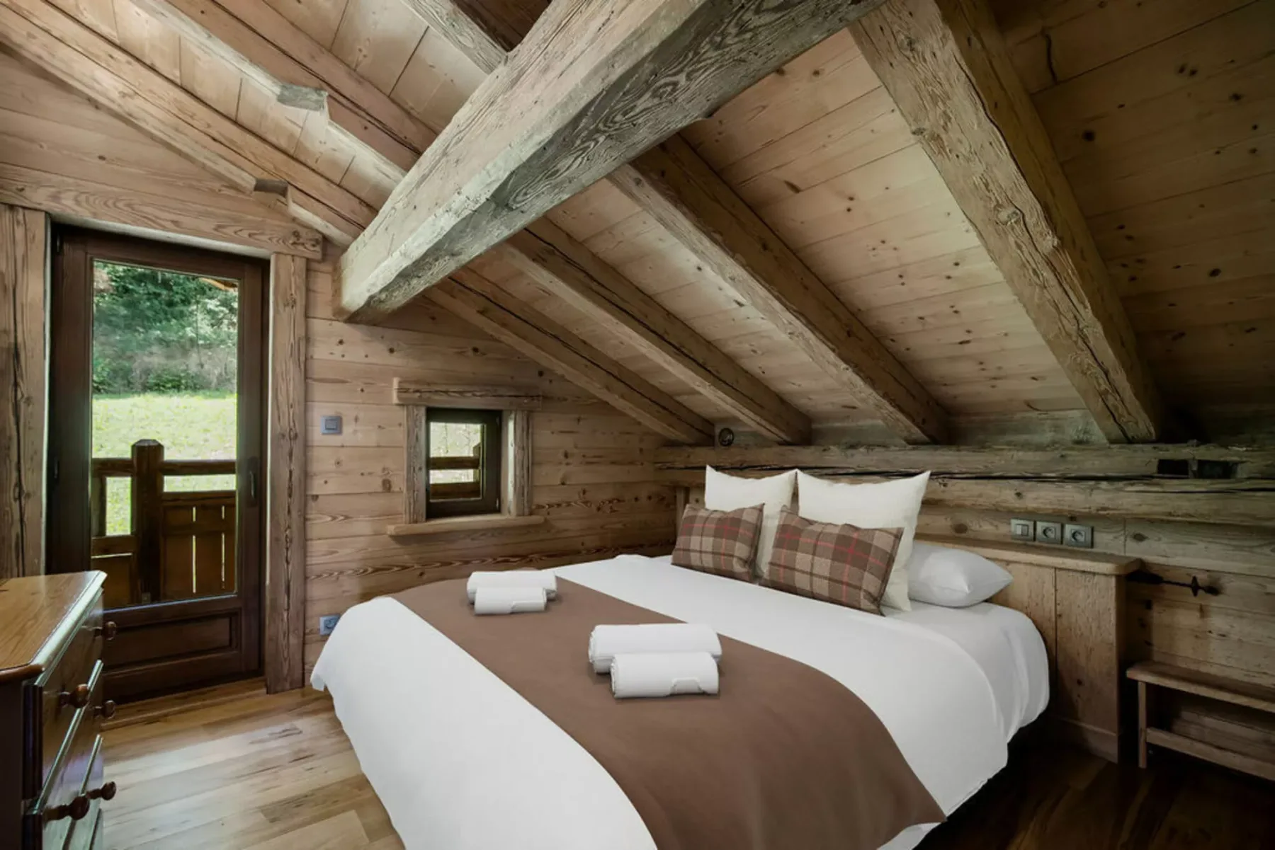 A bedroom with a bed beneath a sloped wooden ceiling and exposed beams.