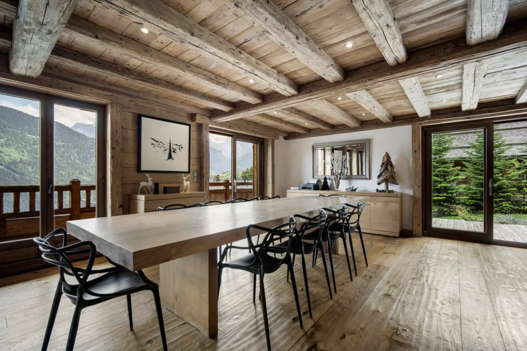 A spacious dining area has a long table, dark seating, and large windows.