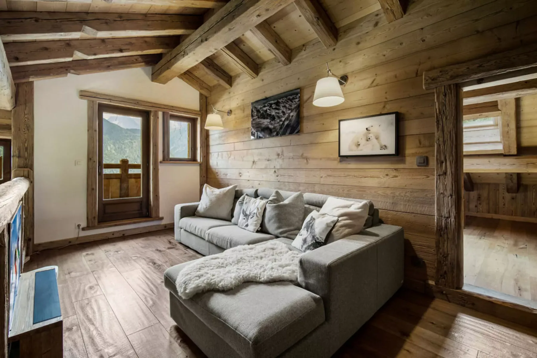 A wood-paneled living room with a sectional sofa beneath exposed ceiling beams.