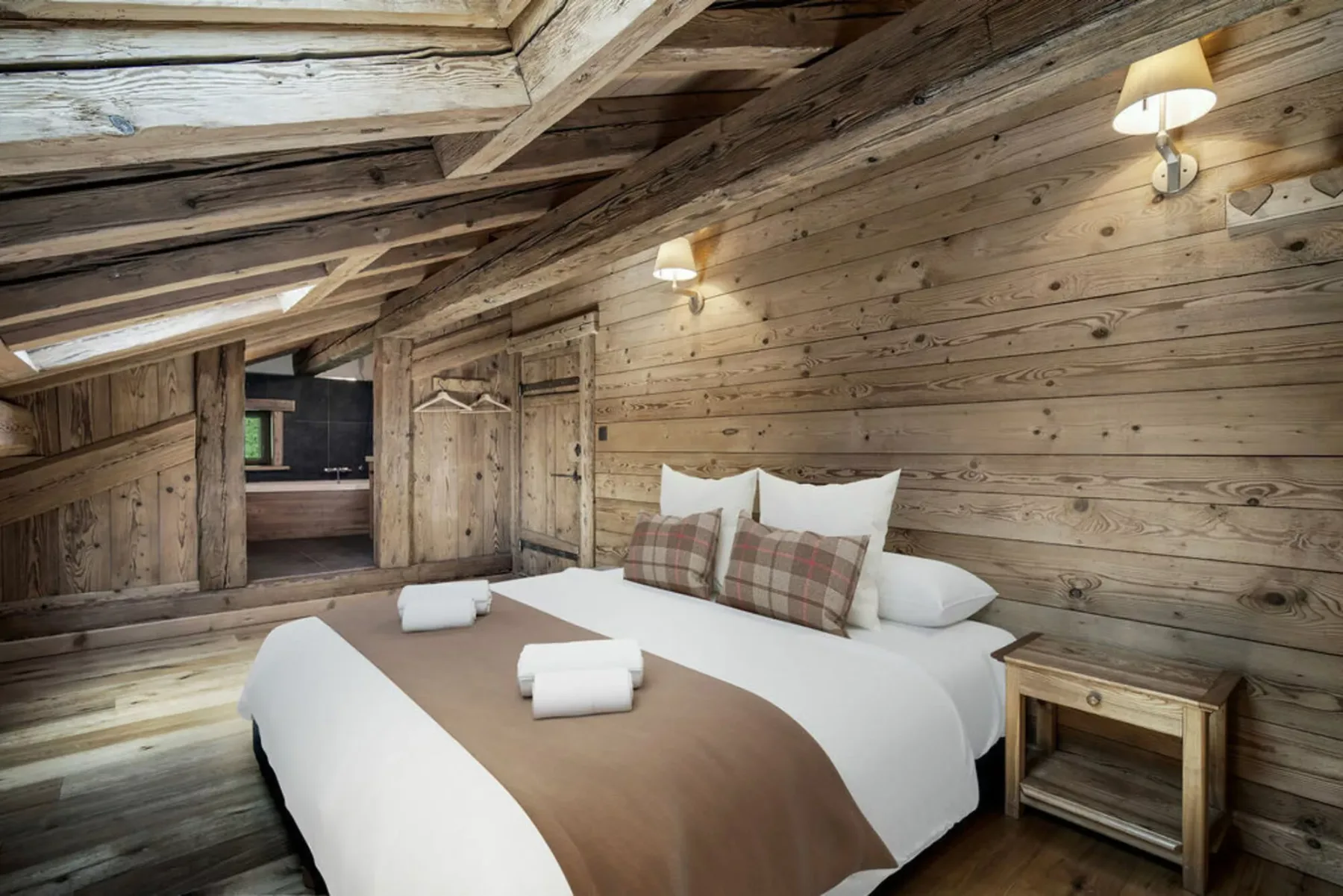 A rustic bedroom with a bed dressed in white linens and plaid pillows.