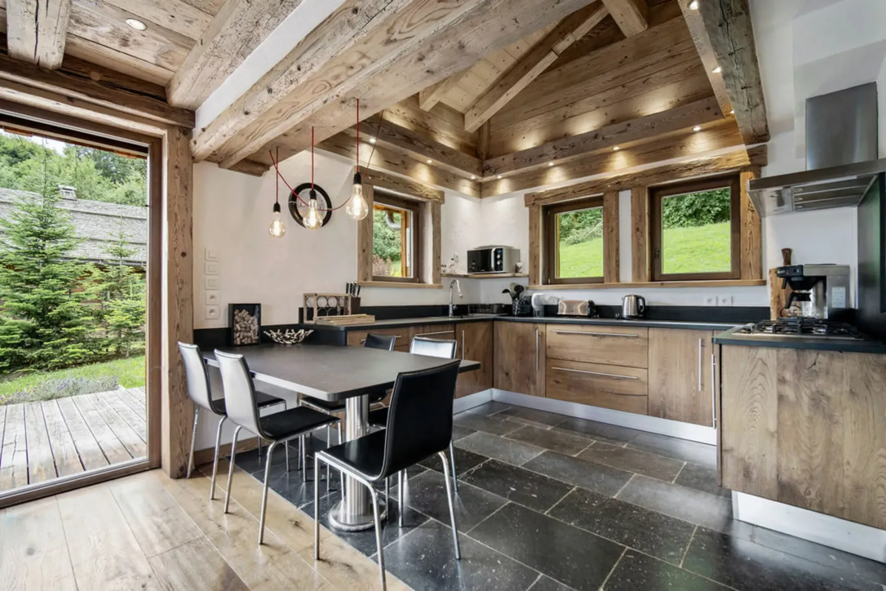 A rustic kitchen and dining area with wooden ceiling beams and large windows.