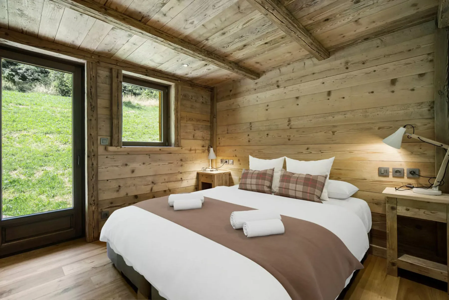 A bedroom with a bed dressed in white linens and wooden walls.