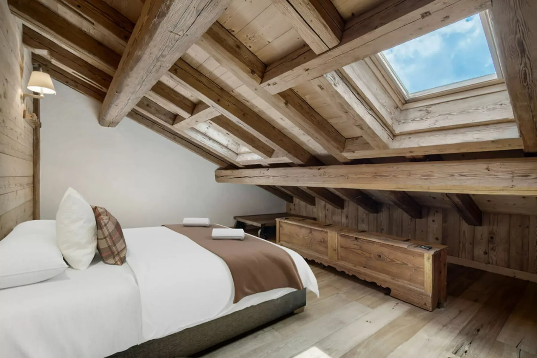 A bedroom with a bed beneath exposed timber beams and skylights.