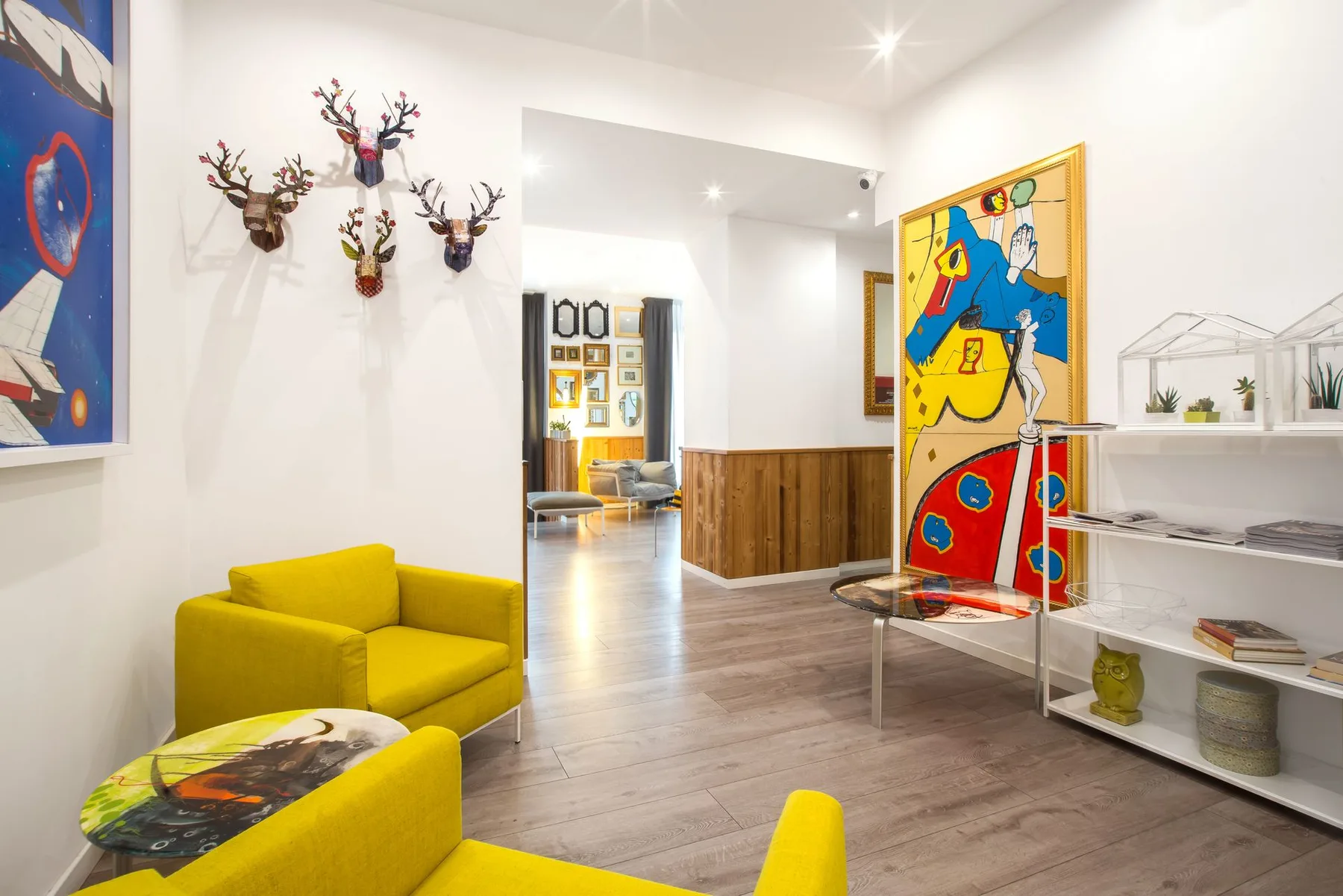 Hotel interior with yellow chairs, artwork, and a wooden reception desk.