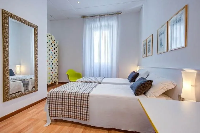 Twin beds in a bright room with a mirror, window, and decorative screen.