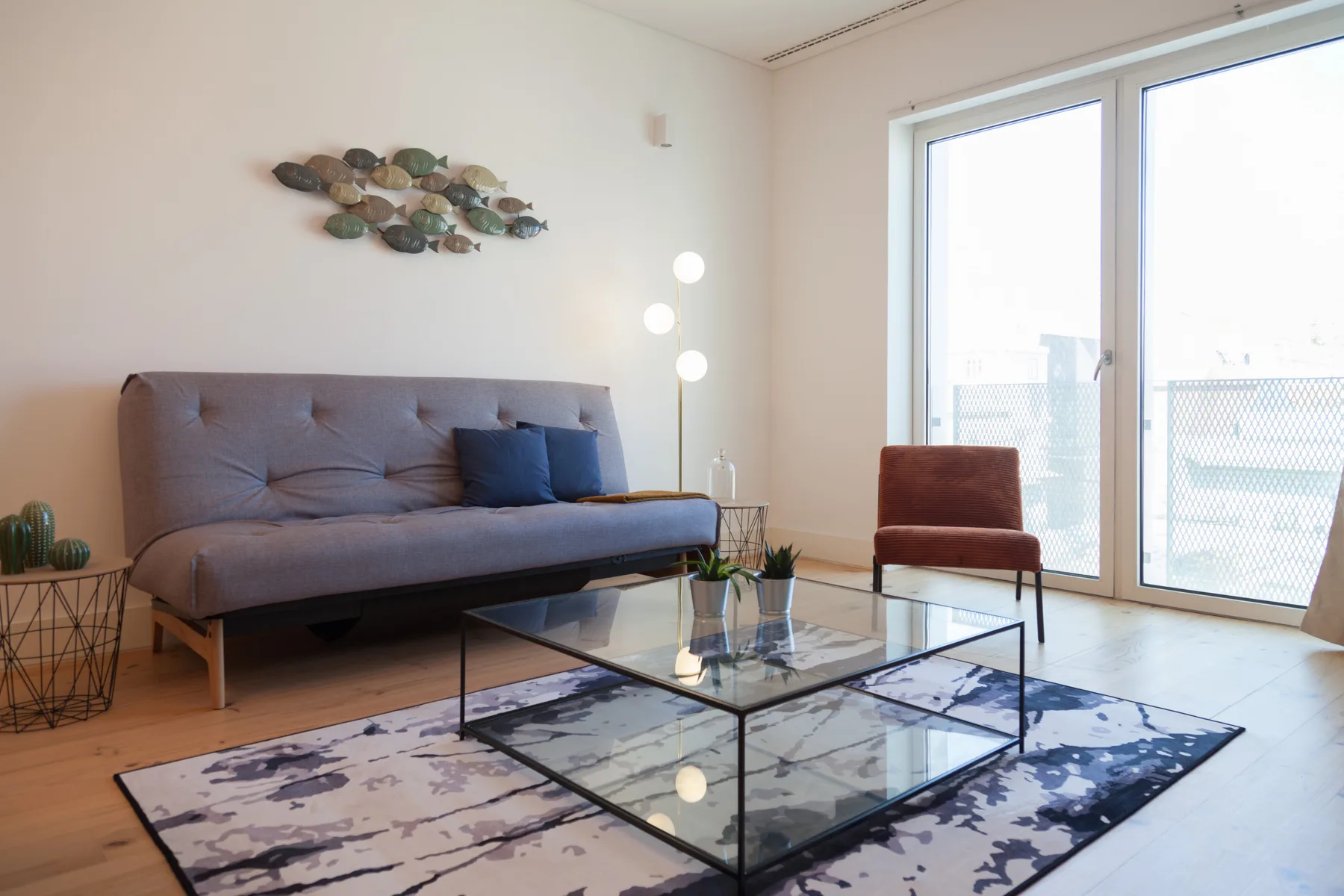 A bright living room with seating and a glass coffee table beside large windows.