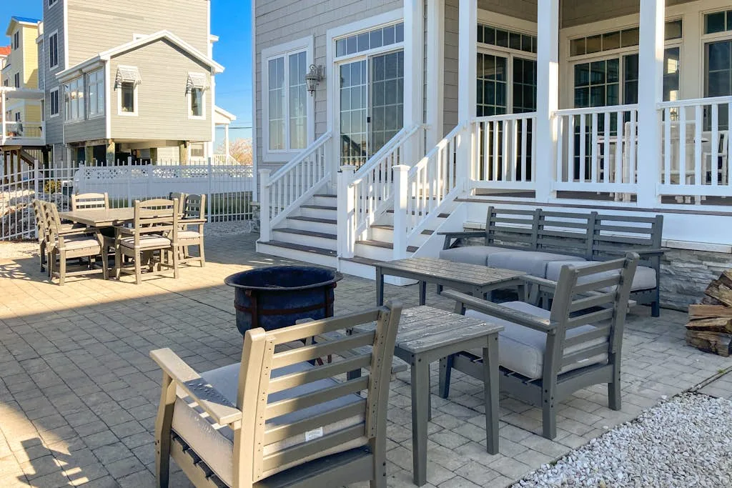 A paved outdoor seating area with wooden furniture beside a white-railed porch.