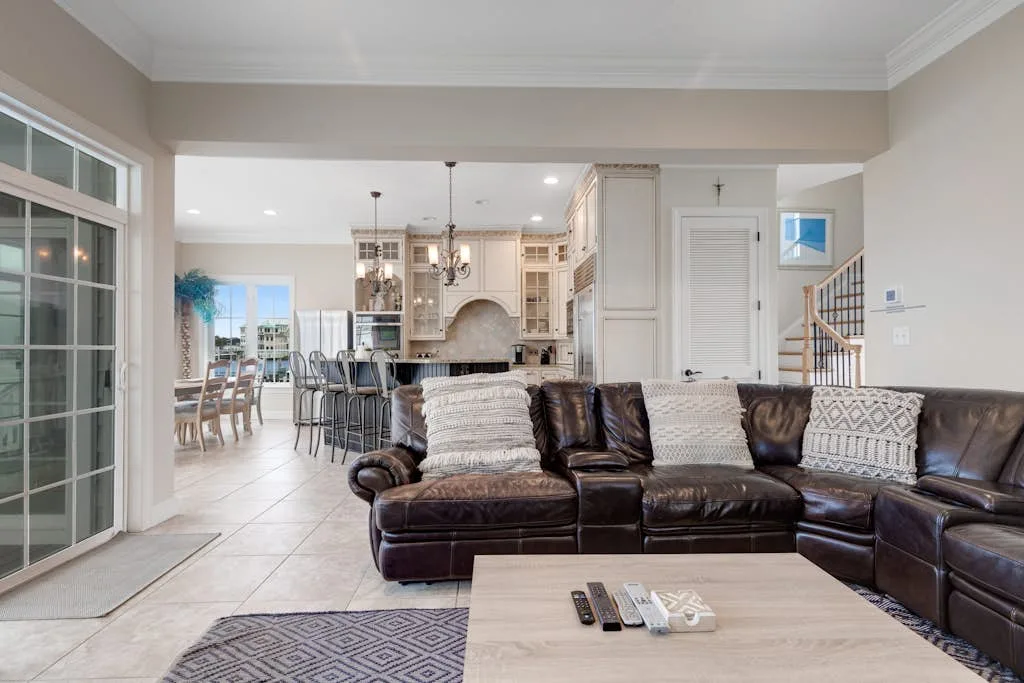 An open-plan living room with dark seating facing a kitchen and dining area.