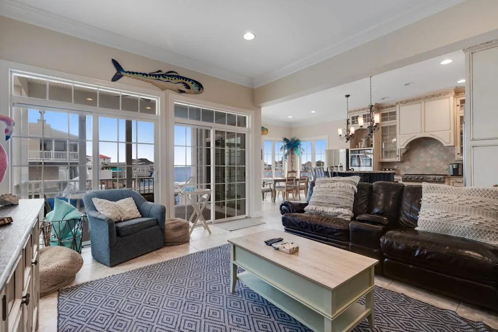 A bright living room with seating, a coffee table, and large windows overlooking the water.