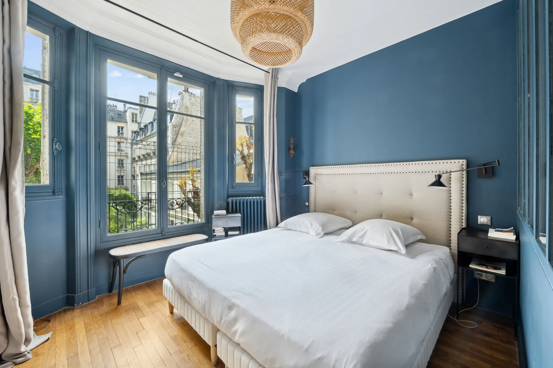 Un dormitorio con una cama blanca junto a ventanas altas con marcos azules.