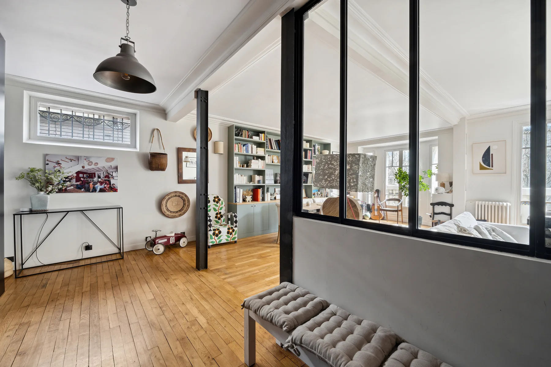 Una luminosa sala de estar con suelo de madera, una estantería y un tabique de vidrio.