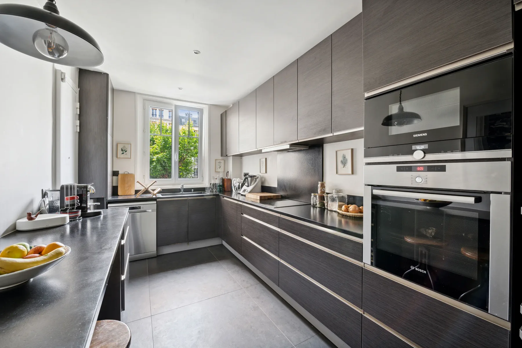 Una cocina moderna con gabinetes oscuros, electrodomésticos de acero inoxidable y una ventana.
