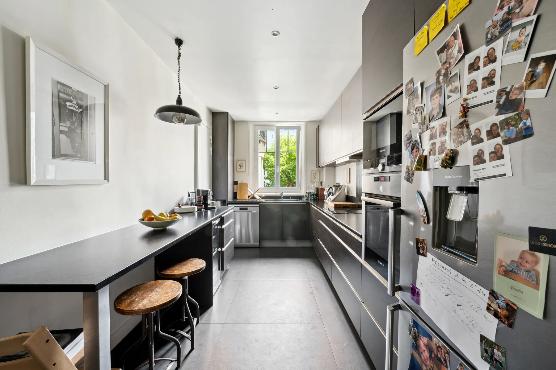 Una cocina moderna con muebles oscuros, una encimera larga y una ventana al fondo.