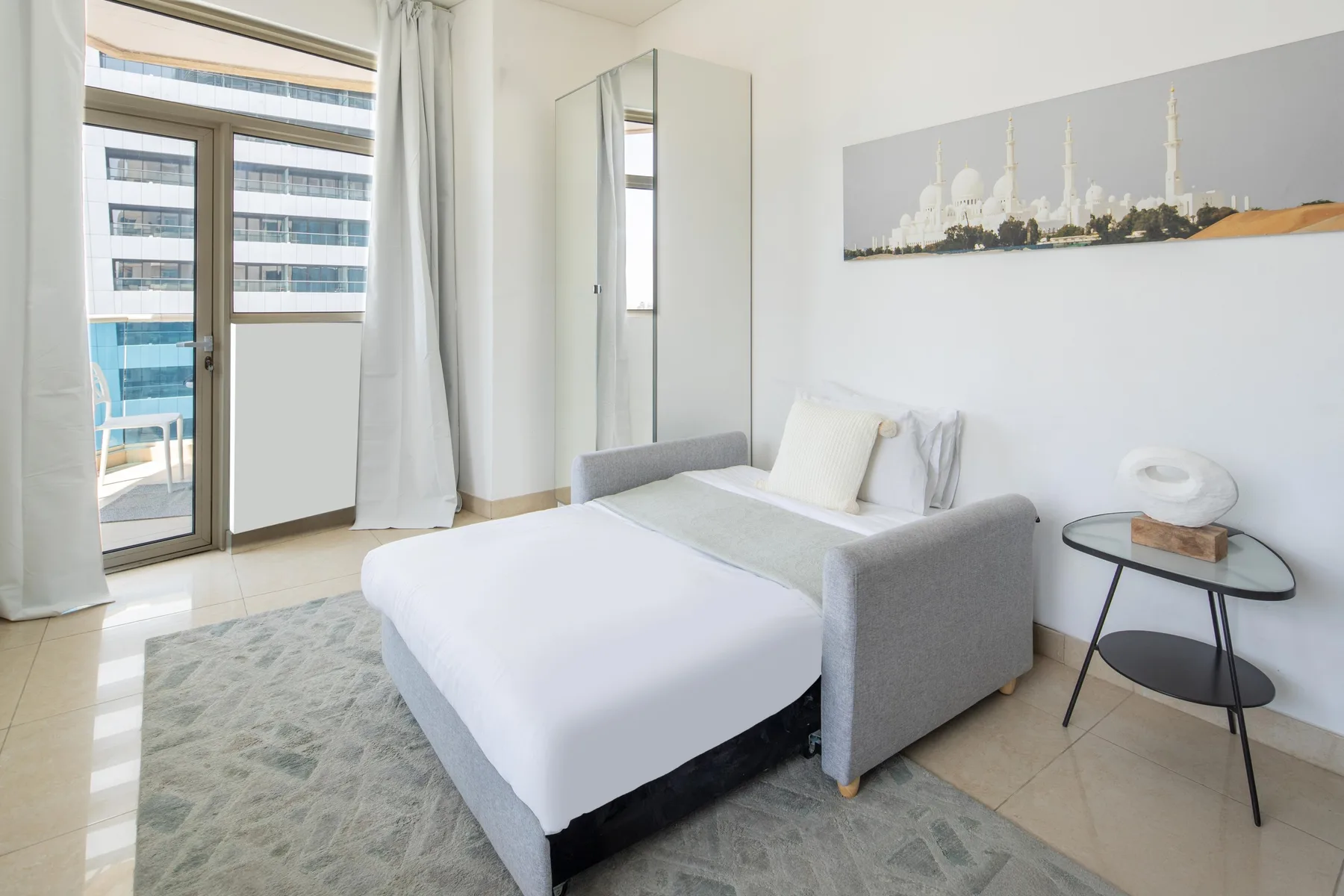 A bright bedroom with a neatly made bed and a glass balcony door.