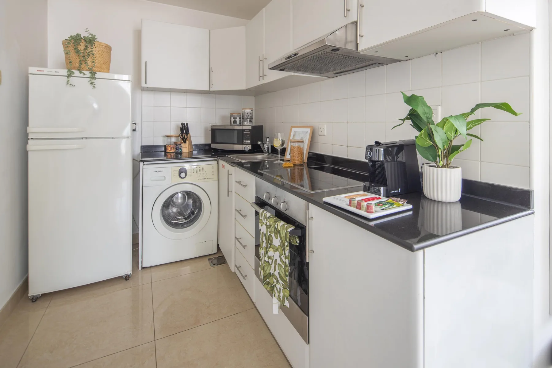 A bright kitchen with white cabinets, dark countertops, and a potted plant.