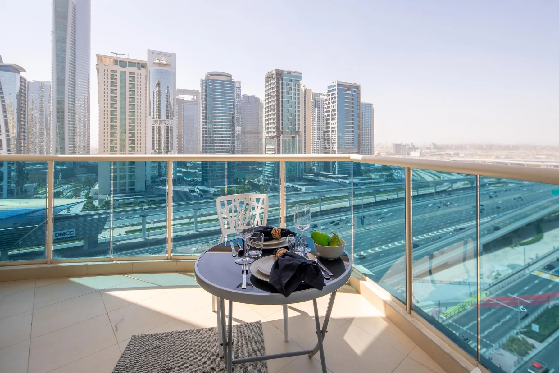 A balcony seating area overlooks a multilane road and surrounding high-rise buildings.
