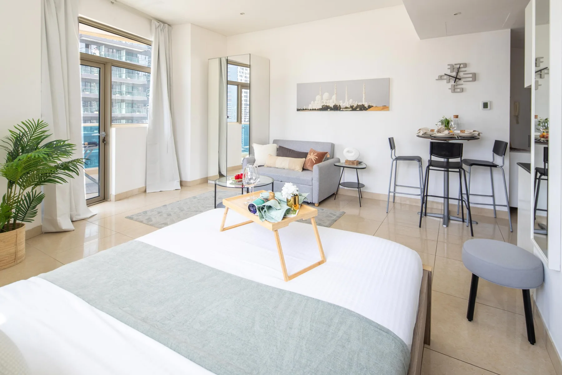 A bright studio living area has a bed, seating, and a small kitchen counter.