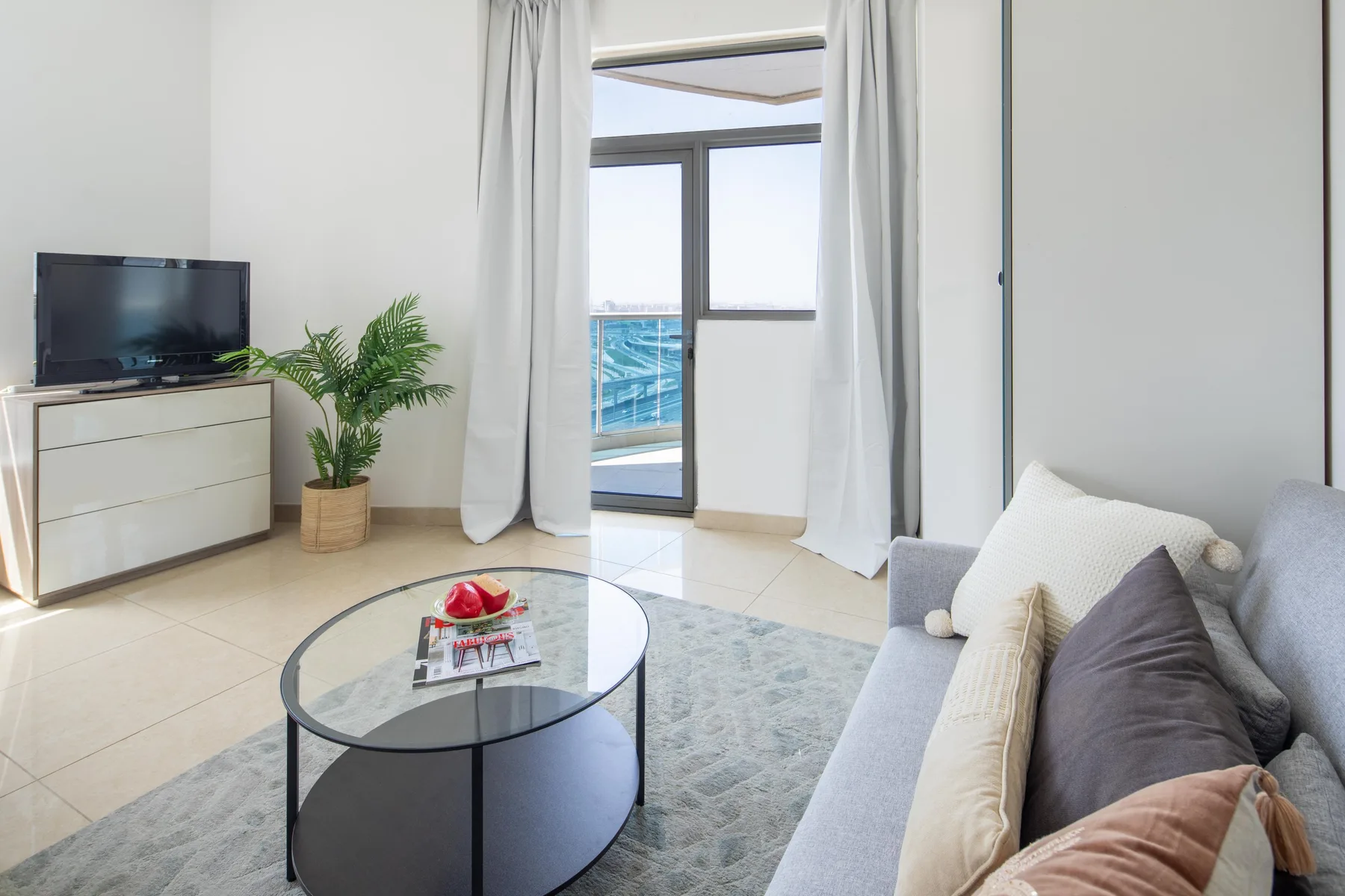 Bright living room with a seating area, television, and glass doors opening to a balcony.