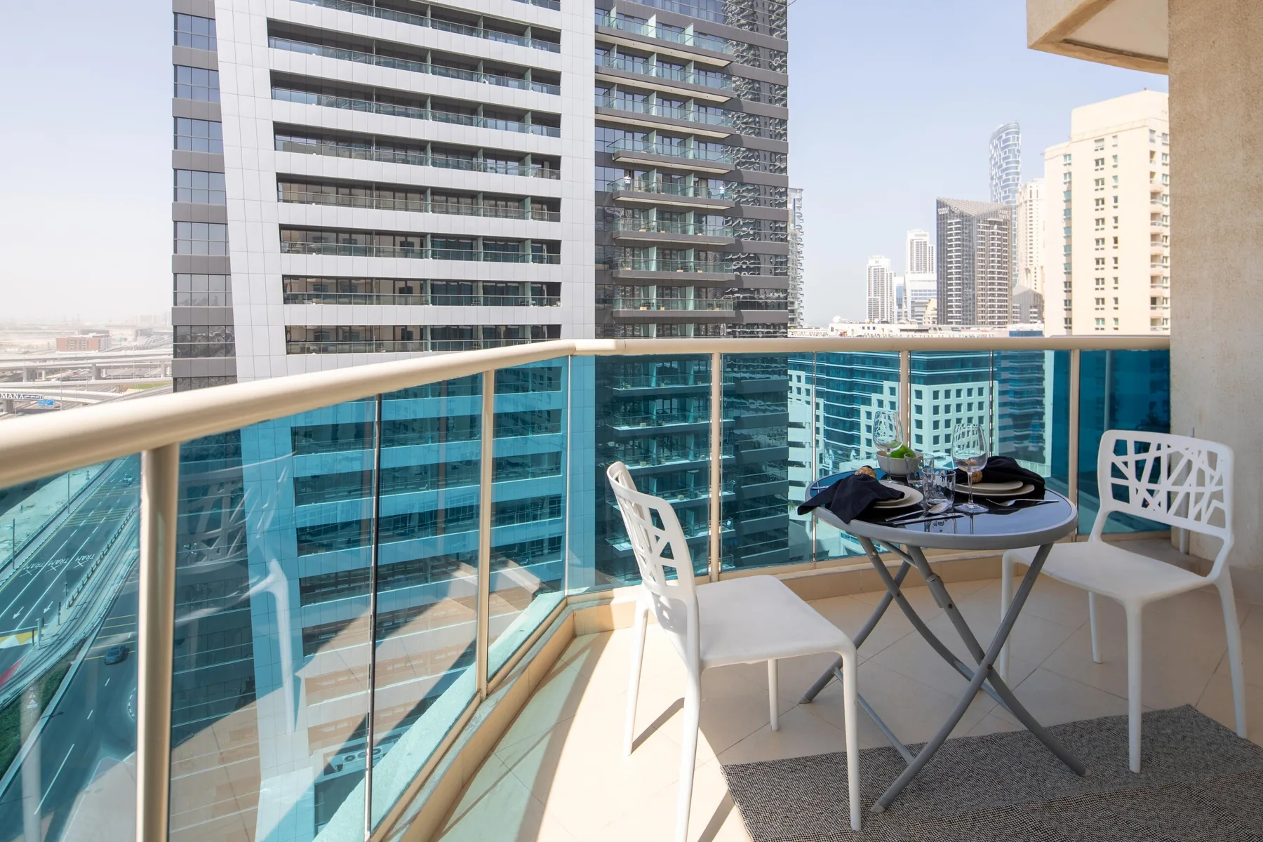A balcony seating area with a small table overlooks nearby high-rise buildings.