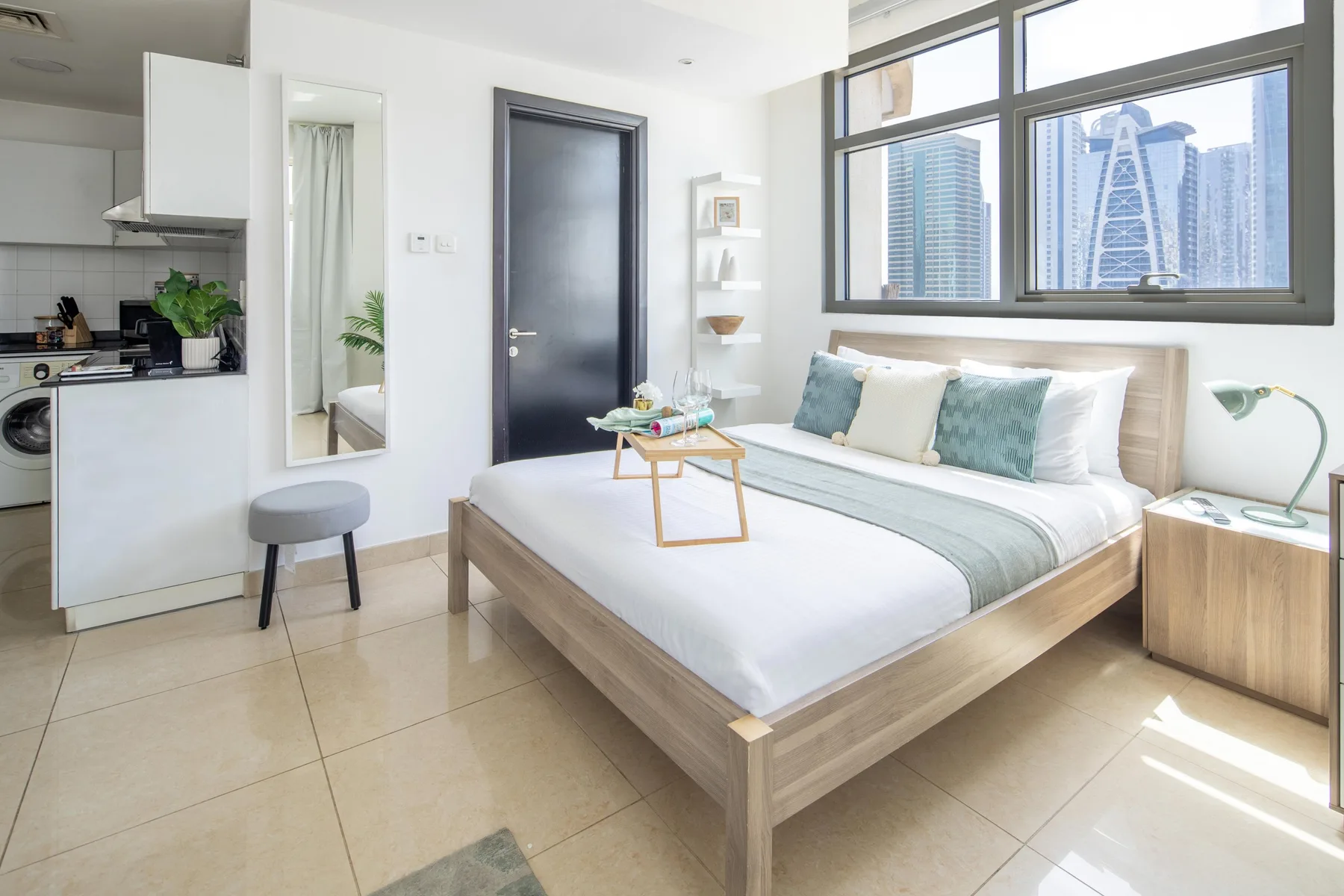 A bright bedroom with a neatly made bed and a large city-facing window.