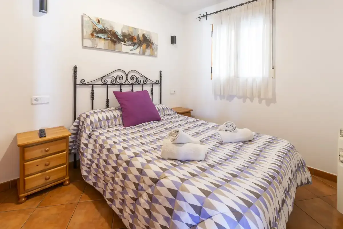 Un dormitorio con una colcha estampada y una ventana con cortinas translúcidas.