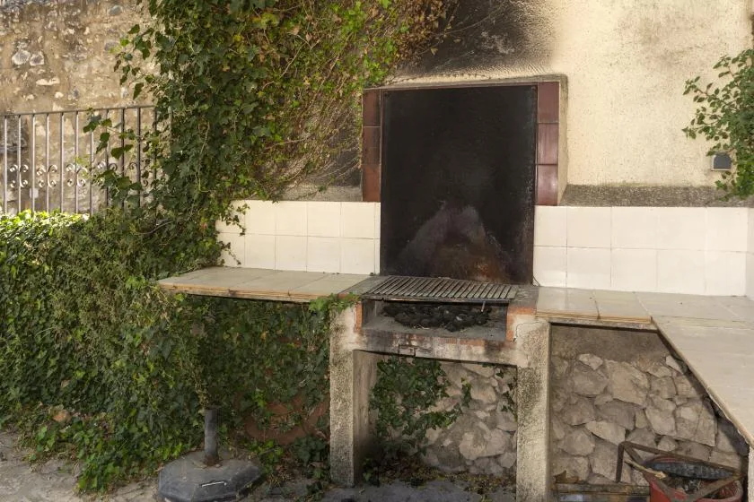 Una parrilla exterior está junto a una pared de azulejos y una encimera de piedra.