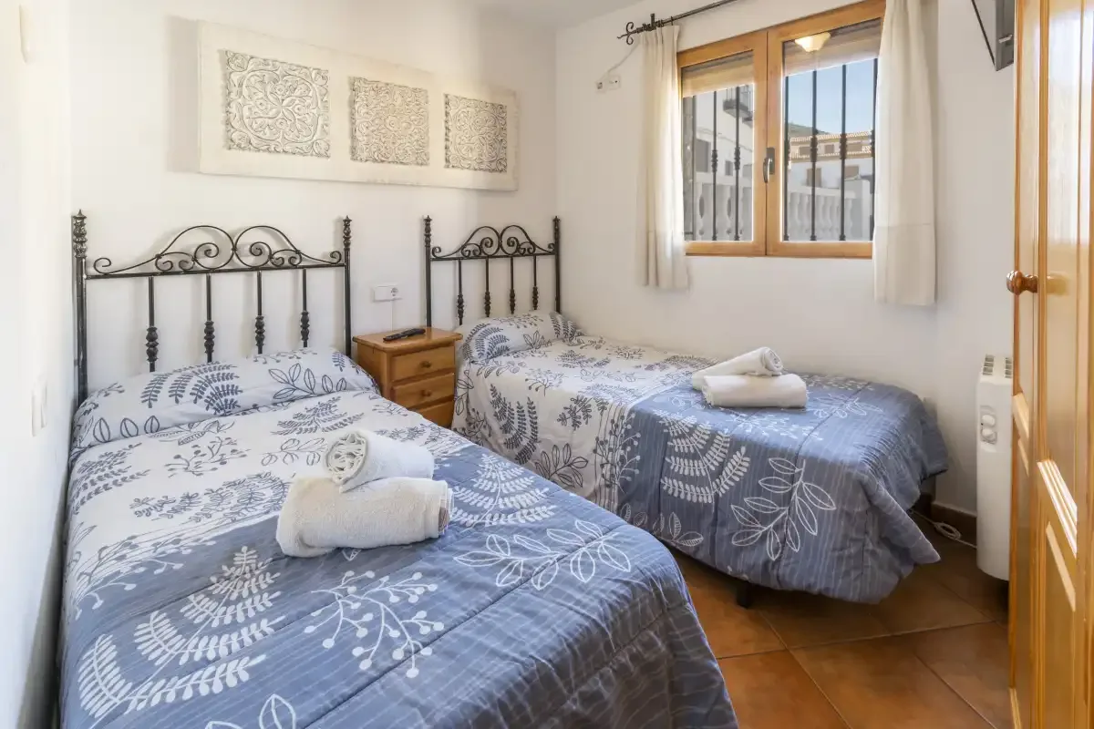 Un dormitorio con dos camas, ropa de cama estampada y una ventana frente a otros edificios.