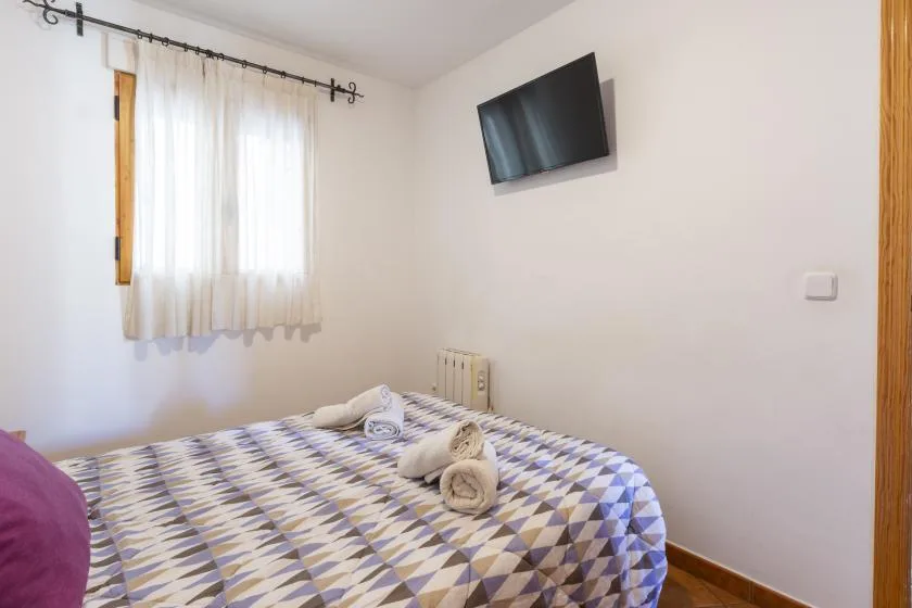 Un dormitorio con una colcha estampada, una ventana con cortinas y un televisor en la pared.