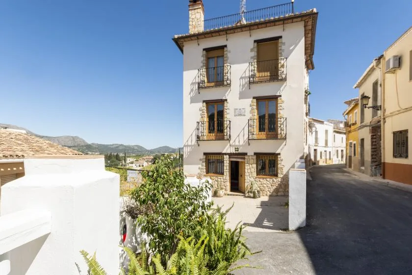 Un edificio blanco y estrecho con balcones da a una calle soleada del pueblo.