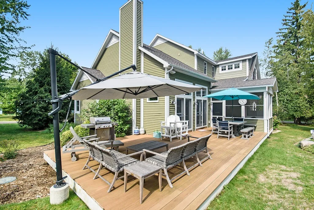 A house patio with outdoor seating and umbrellas beside a lawn.