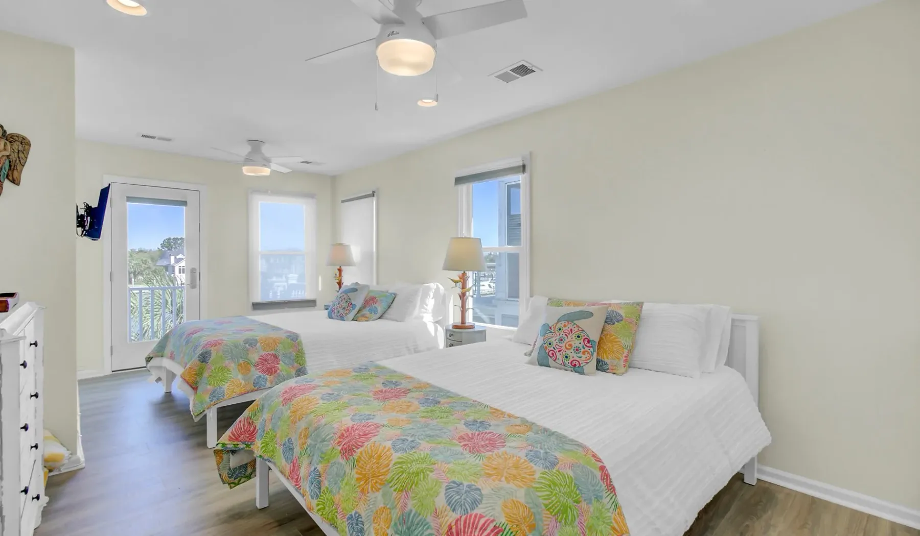 Un dormitorio luminoso con ropa de cama blanca y colchas florales coloridas.