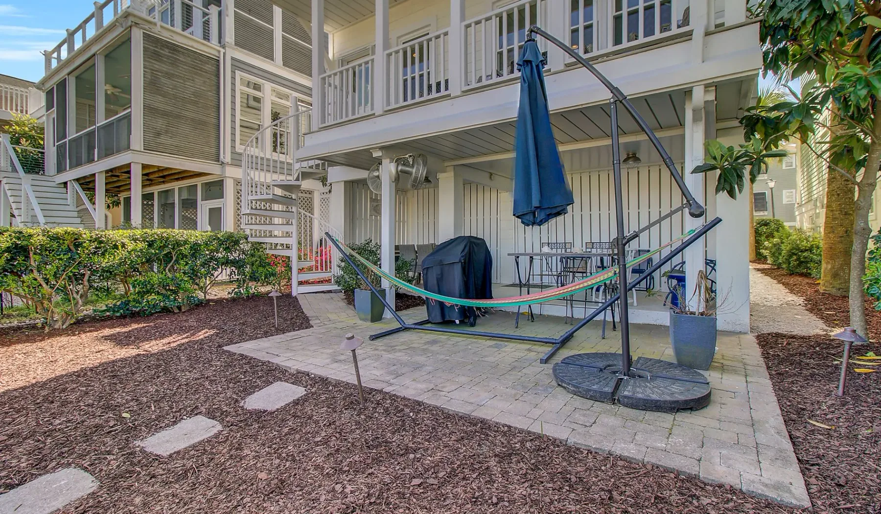 Un patio bajo una casa elevada tiene una hamaca y asientos al aire libre.
