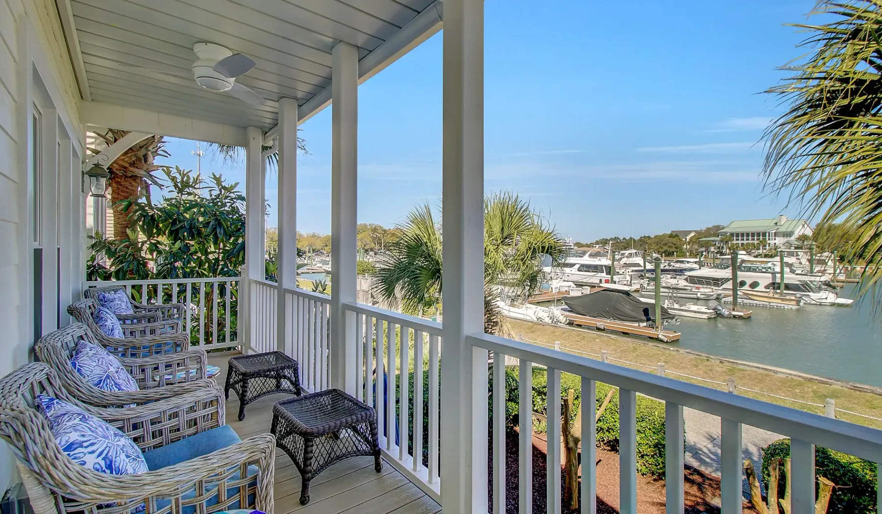 Un porche cubierto con asientos acolchados da a una marina con barcos.