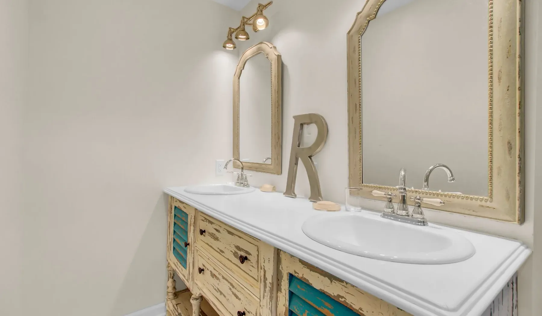 Un tocador de baño con una encimera blanca larga, dos lavabos y espejos enmarcados.