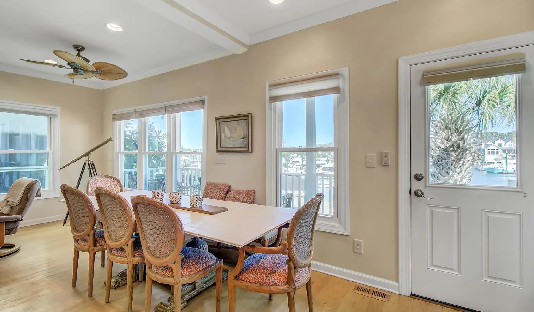Un comedor luminoso con una mesa y sillas tejidas junto a grandes ventanas.