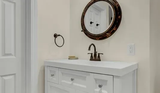 Un tocador blanco de baño está debajo de un espejo ovalado.