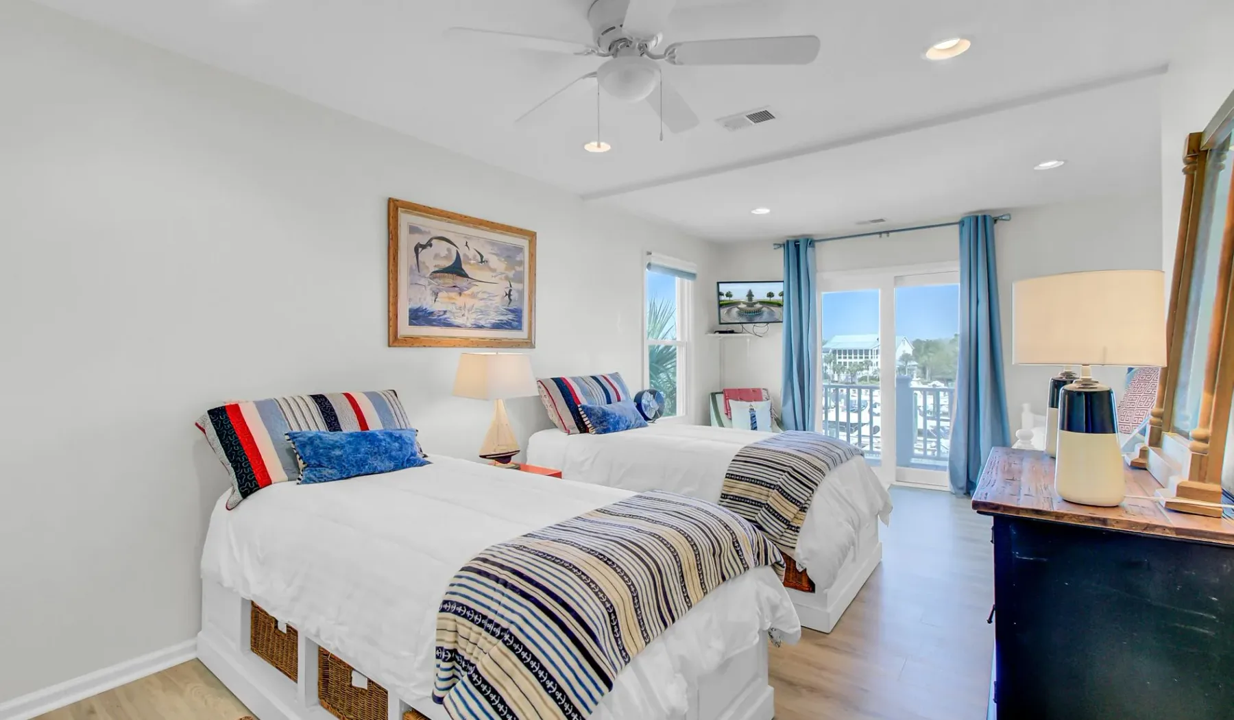 Un dormitorio luminoso con dos camas, ropa de cama a rayas y cortinas azules junto a las ventanas.