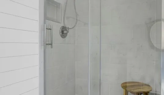 Una ducha de baño con azulejos, cabezal de mano y taburete de madera.