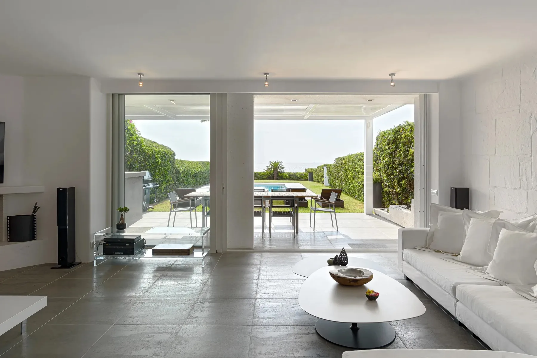A bright living room opens onto a patio with outdoor seating and greenery.