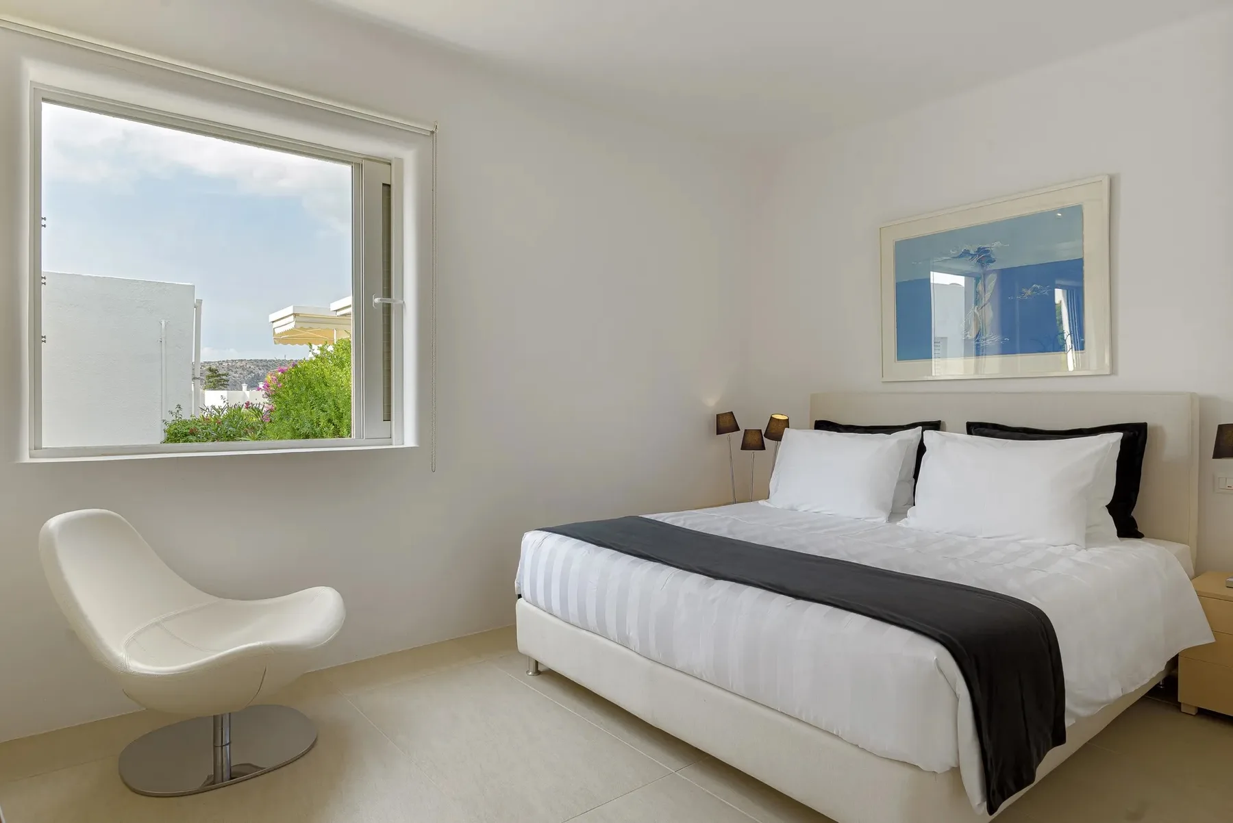 A bright bedroom with a large bed and a window overlooking greenery.