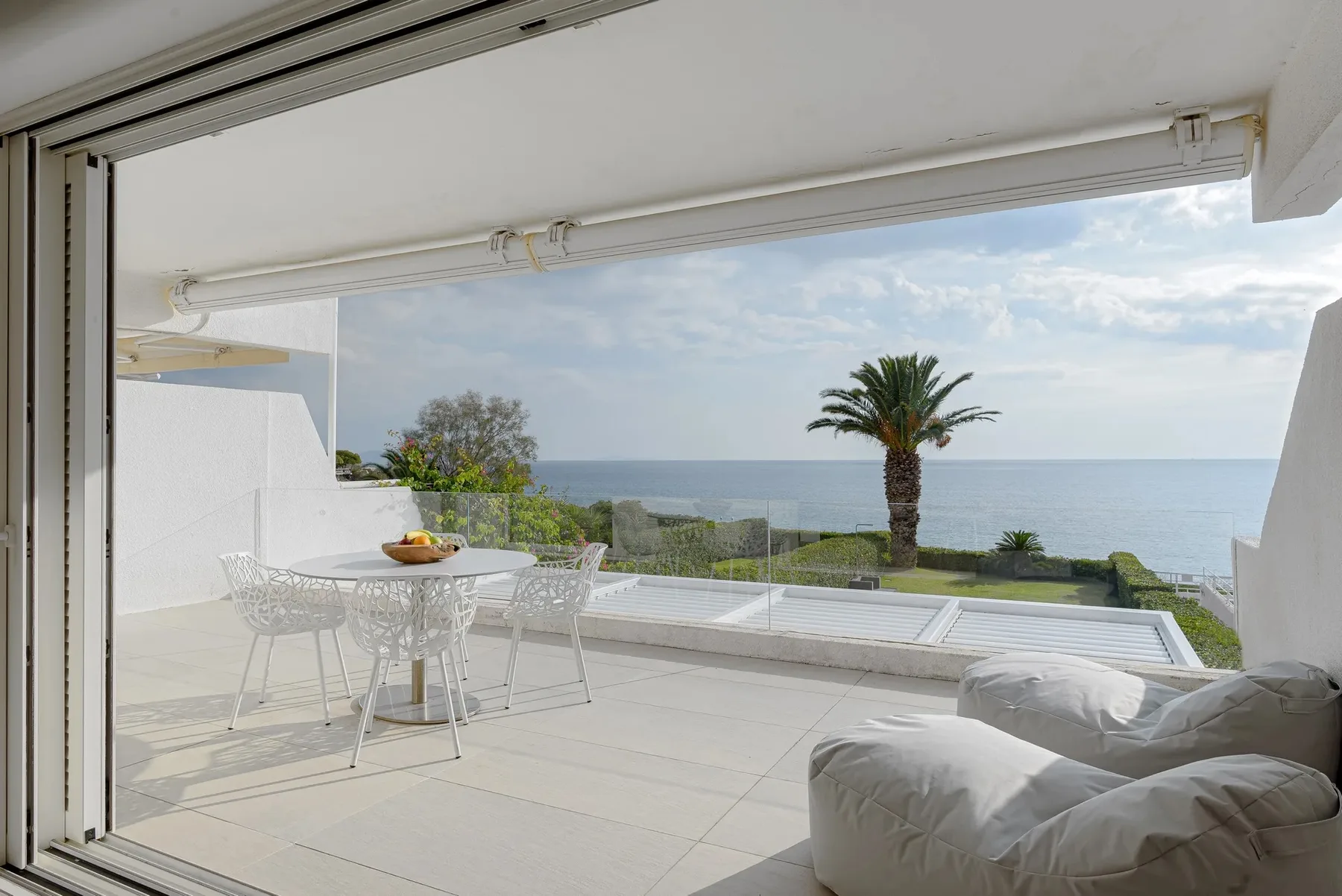 A bright terrace opens onto a sea view, with a table and seating.