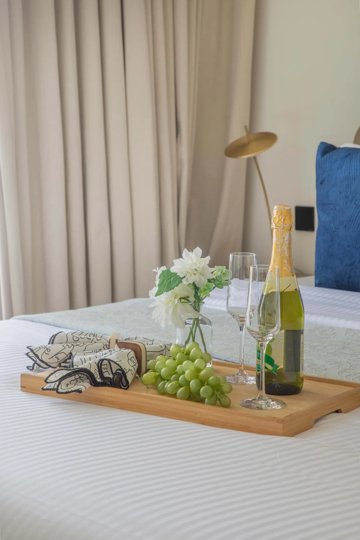 A bedroom table is set with green grapes, flowers, glasses, and a bottle.