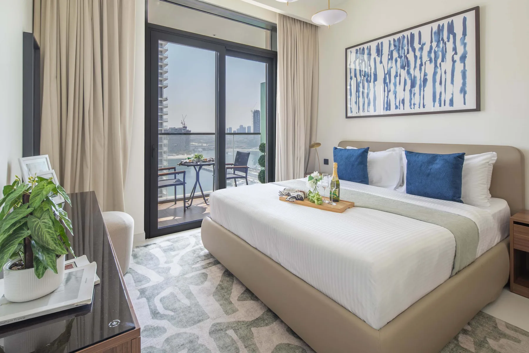 A bright bedroom with a neatly made bed beside a large window overlooking the water.