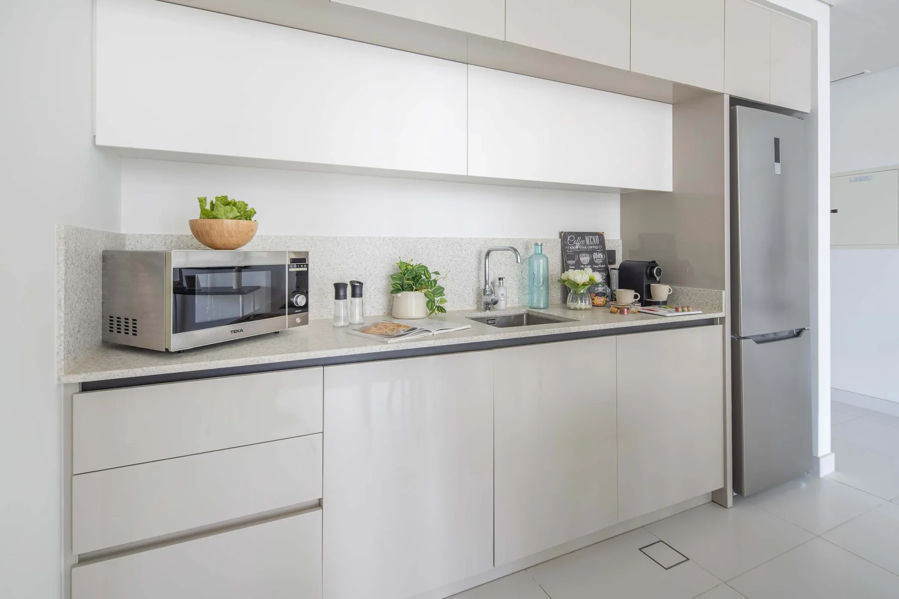 A modern kitchen with white cabinets, a countertop, and a refrigerator.