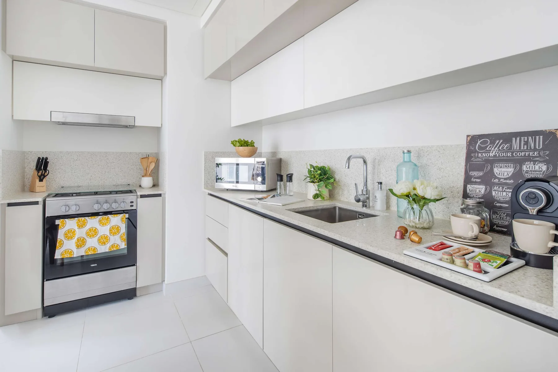 A bright white kitchen with a long counter, sink, and stove.