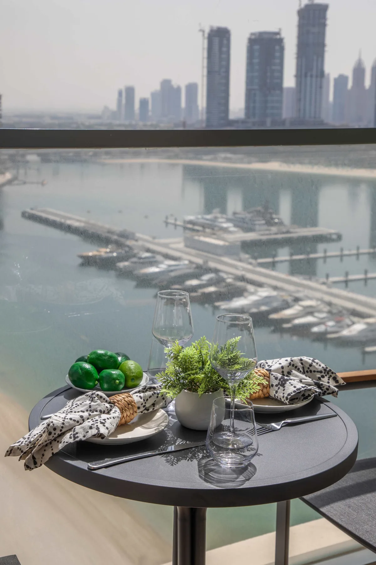 A dining table with greenery and place settings overlooks a marina and city skyline.