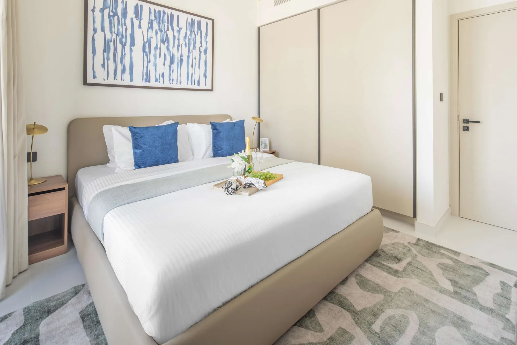 A bright bedroom features a neatly made bed and blue accent pillows.