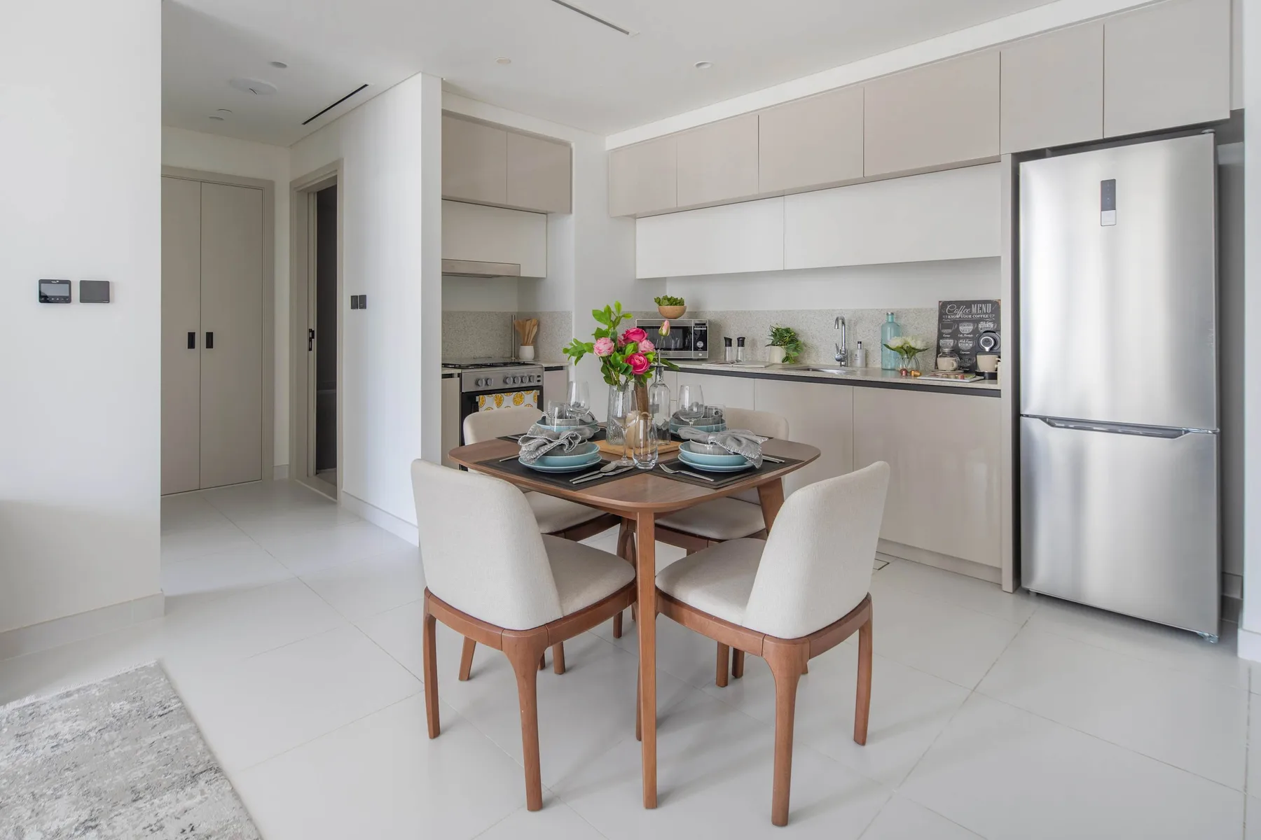 A dining table is set in a bright kitchen with light cabinetry.