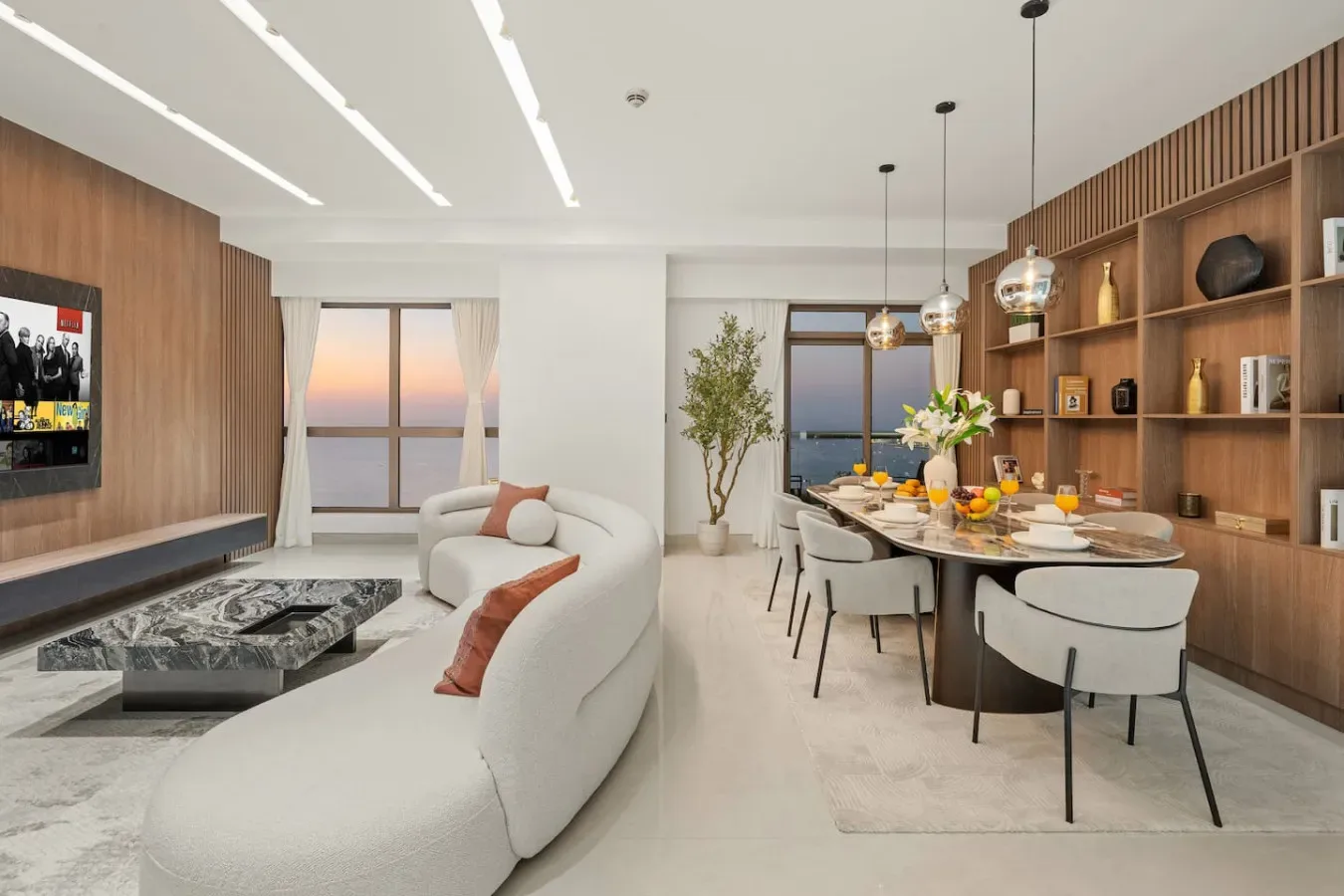 Sala de estar y comedor de planta abierta, con asientos curvos y una mesa de comedor larga.