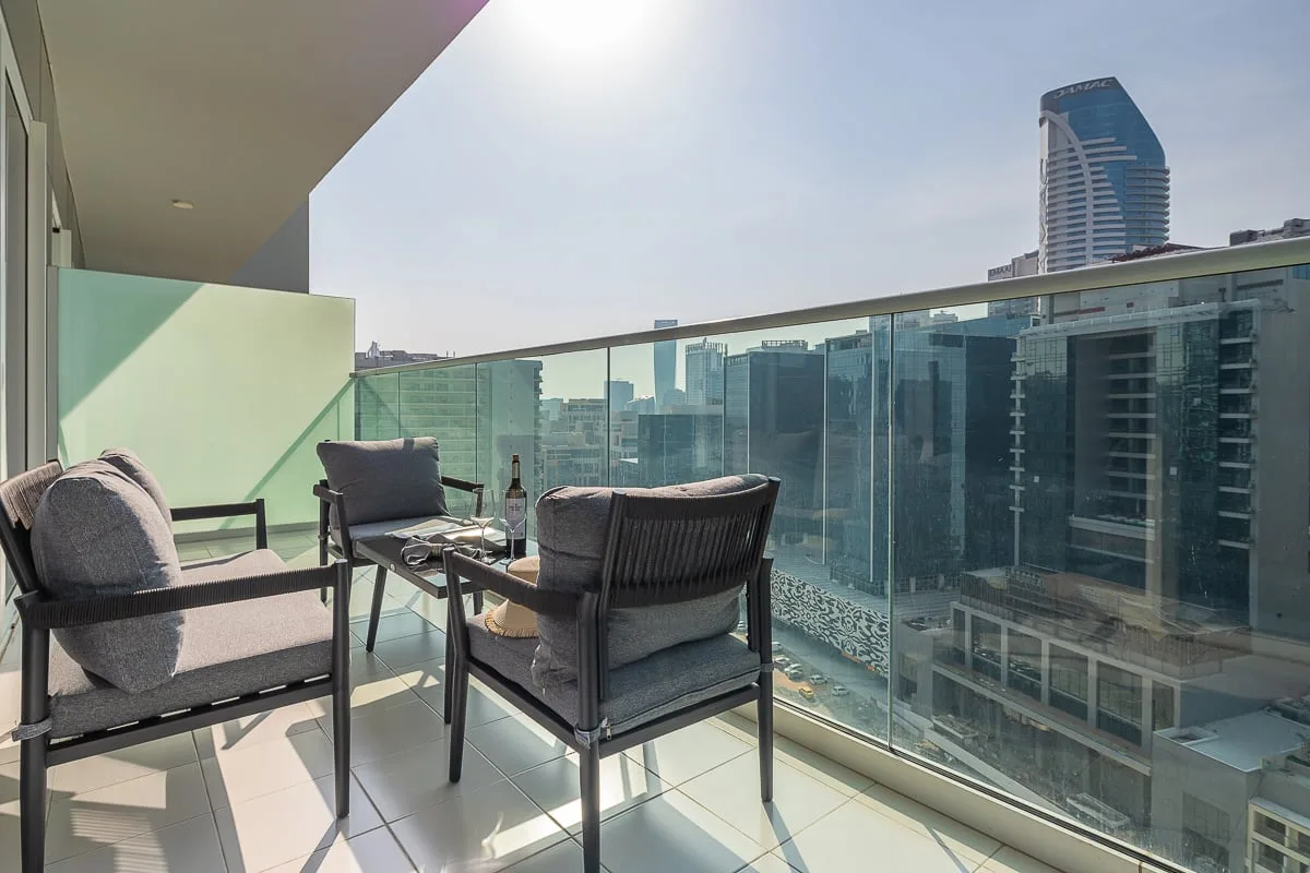 A balcony seating area overlooks a city skyline through a glass railing.